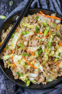 Colorful egg roll in a bowl with ground meat, shredded cabbage, and carrots, garnished with green onions and sesame seeds