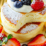 Japanese Soufflé Pancakes: A Fluffy Breakfast Treat for Busy Parents 4 Stack of tall, fluffy Japanese soufflé pancakes dusted with powdered sugar and topped with butter, served on a white plate